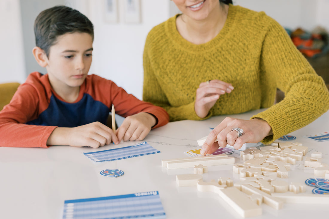 Young boy watches mother select a wooden game piece from SimplyFun's Asymbol, a 3D building game for ages 8 and up