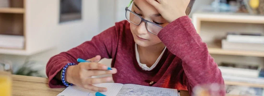 Child in red shirt nervoously looking at notebook while holding a blue pen