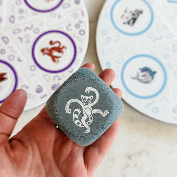 Dance Like a Lemur game from SimplyFun. Featuring a colorful box with playful lemur illustration and foam game puzzle pieces and die with a variety of animal and icon imagery. -SimplyFun