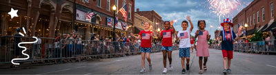 Children in patriotic outfits walking down a street with fireworks in the background