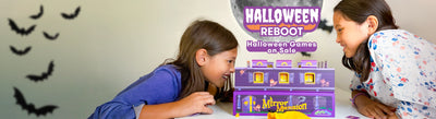 Two children sitting at a table playing with a SimplyFun's Mirror Mansion board game, with black bat cutouts on the wall behind them.