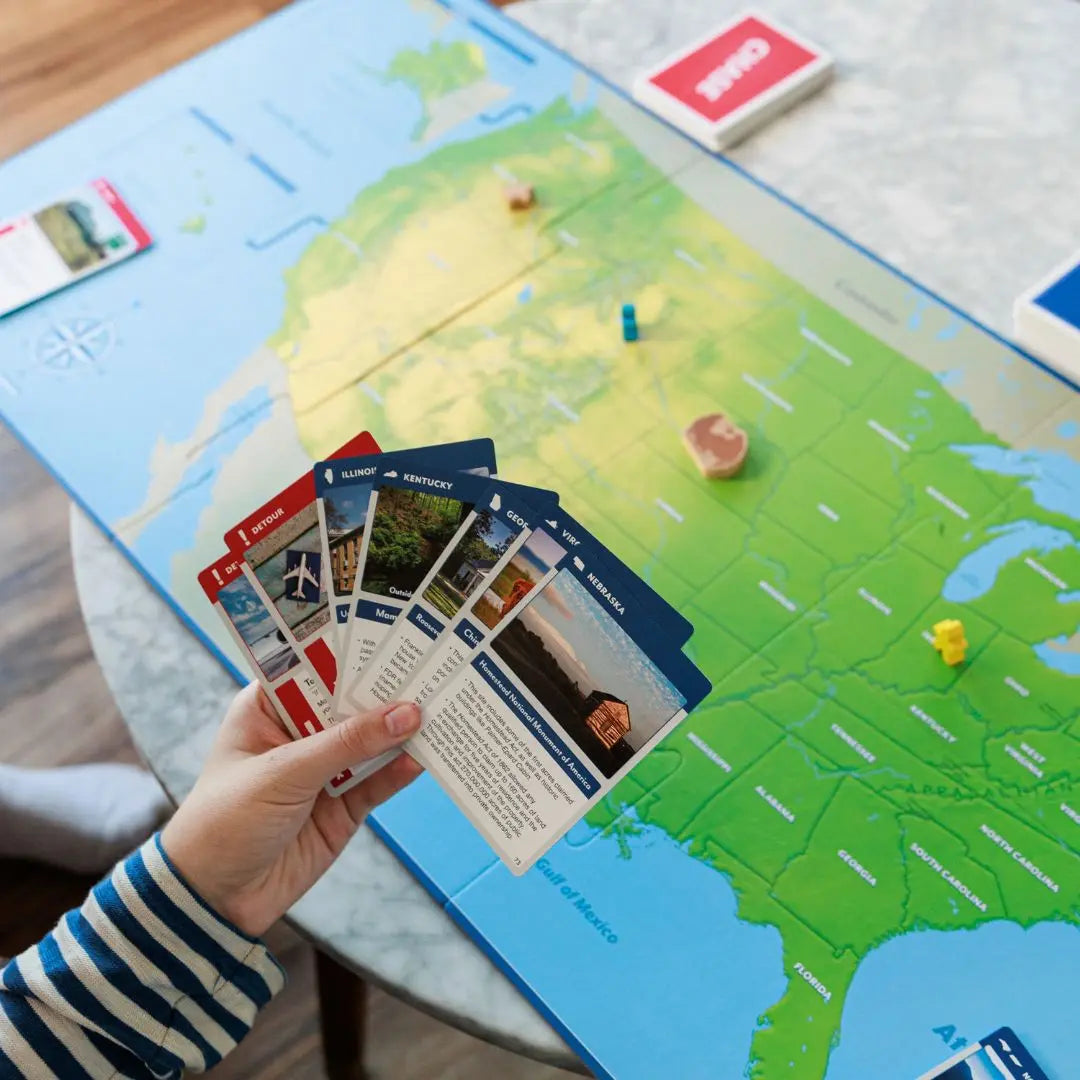 Person holding travel-themed cards over a map of the United States in the board game Eagle Chase-SimplyFun