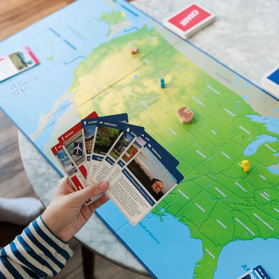 Person holding travel-themed cards over a map of the United States in the board game Eagle Chase